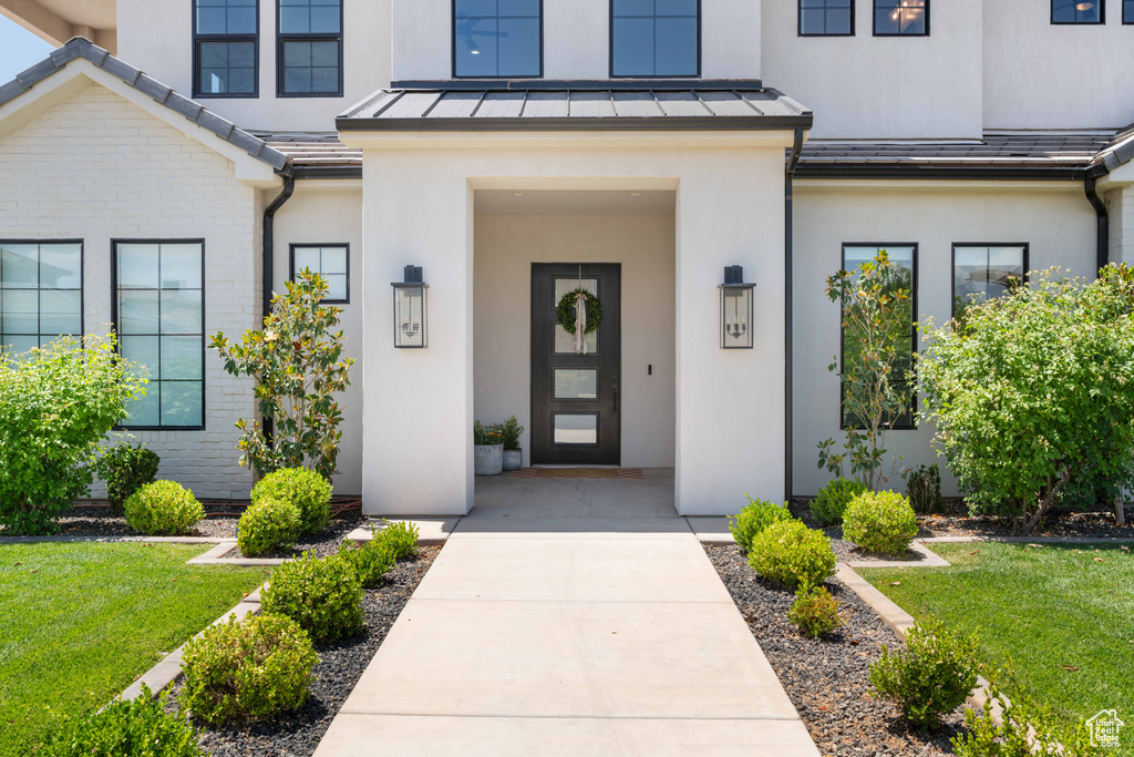 View of exterior entry with a standing seam roof, stucco siding, a yard, and metal roof