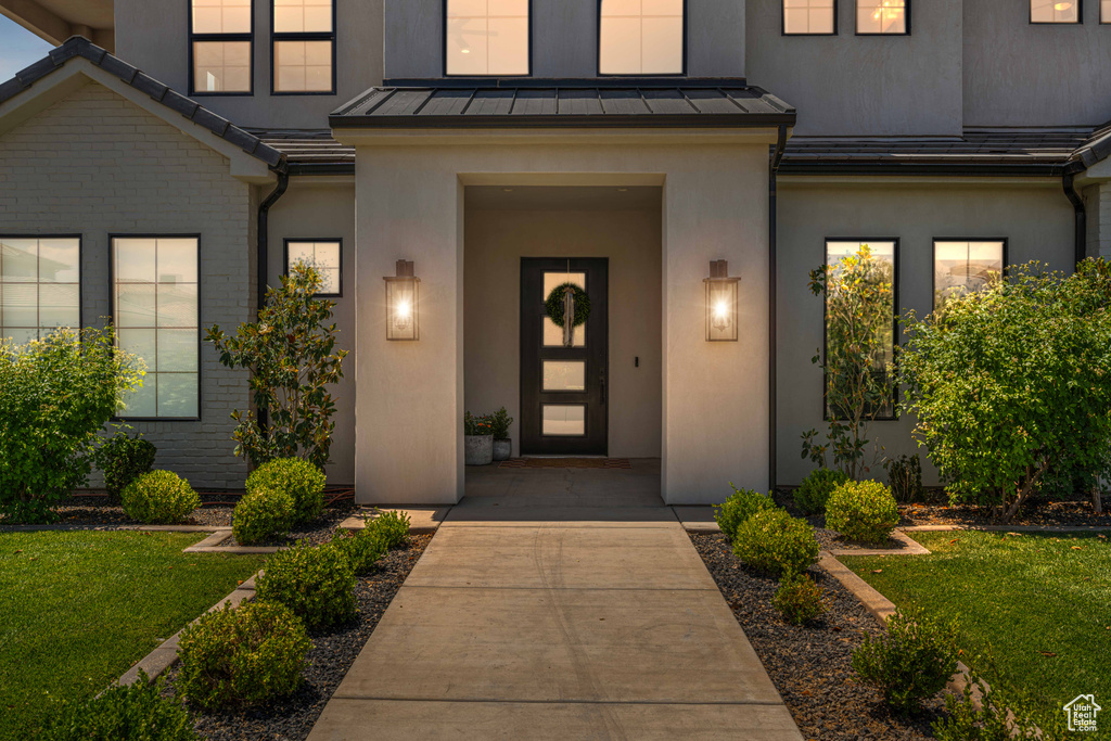 Doorway to property featuring a standing seam roof, stucco siding, a lawn, and metal roof