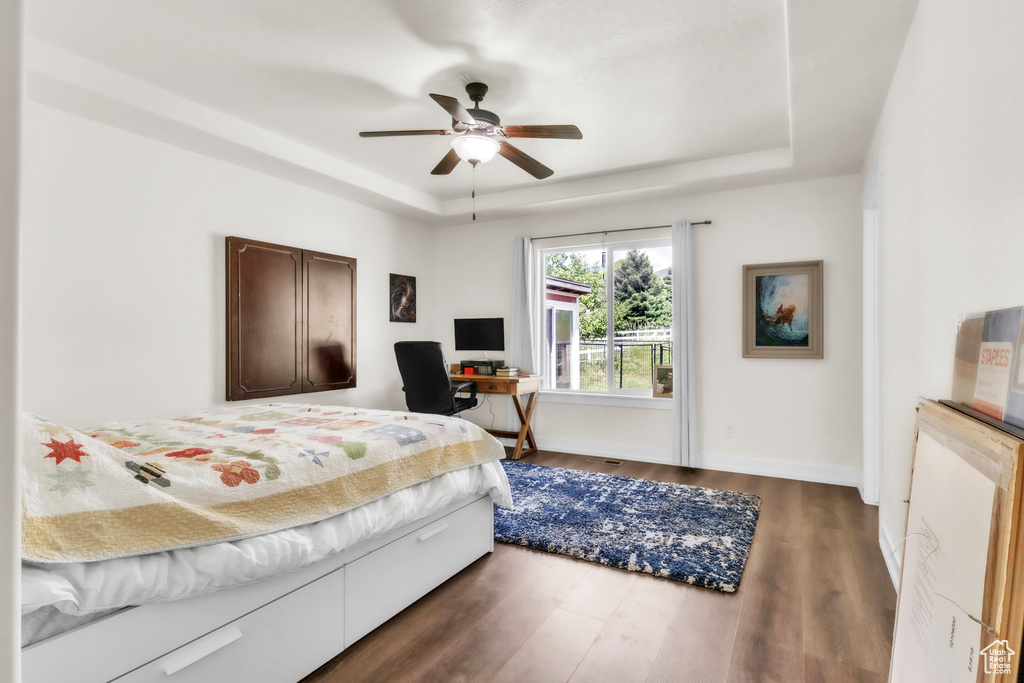 Bedroom with a raised ceiling, wood finished floors, baseboards, ceiling fan, and a desk