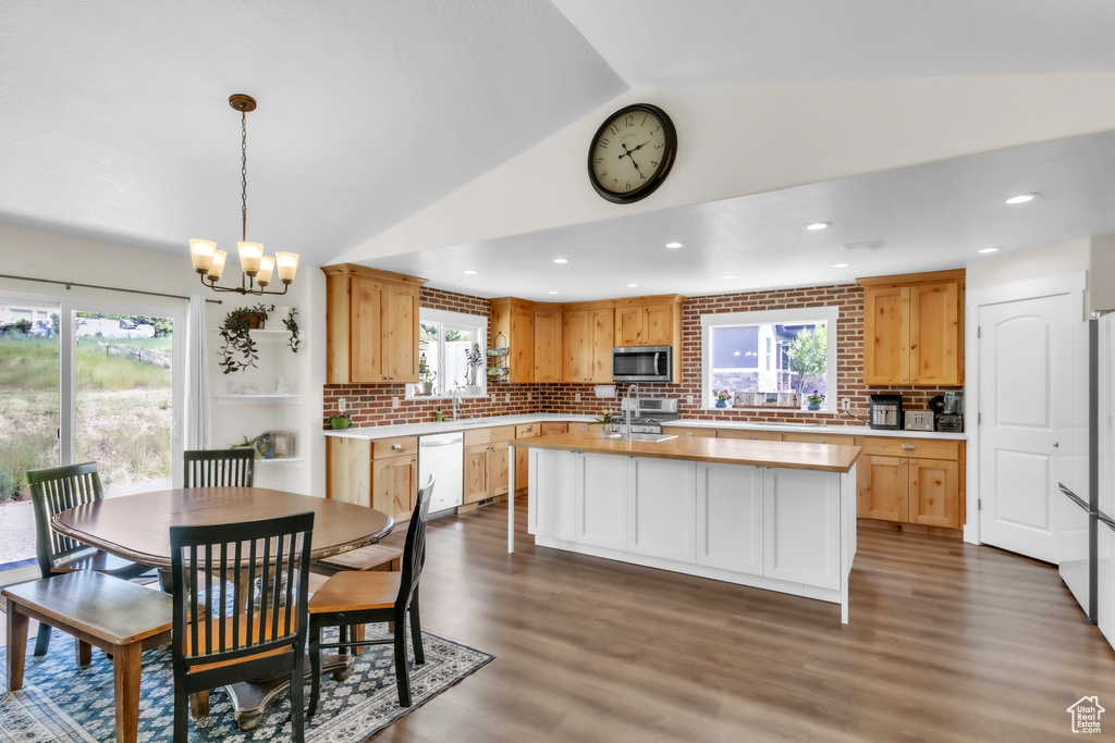 Kitchen featuring stainless steel microwave, vaulted ceiling, light countertops, white dishwasher, and tasteful backsplash