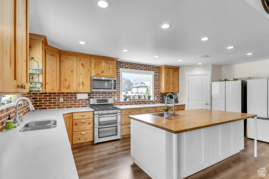Kitchen featuring appliances with stainless steel finishes, a sink, wooden counters, a kitchen island with sink, and recessed lighting