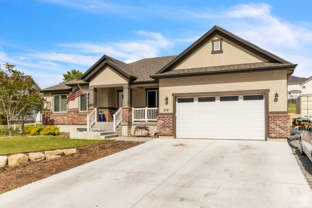View of front of property with brick siding, stucco siding, a porch, a garage, and driveway