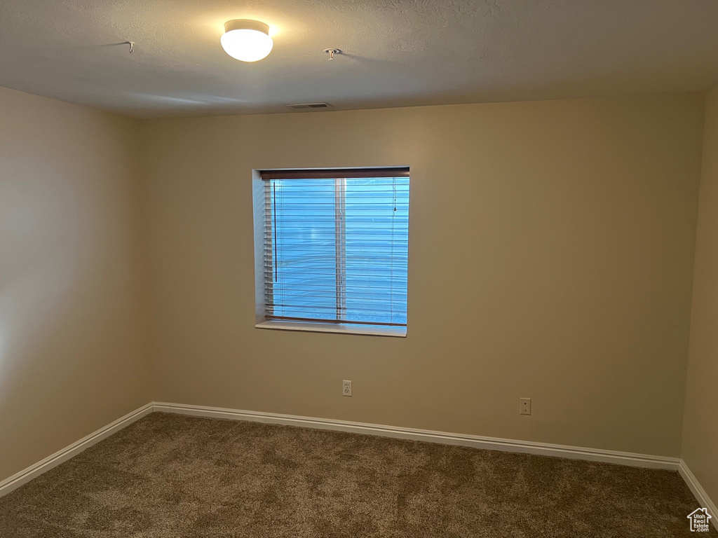 Spare room featuring dark carpet, baseboards, and fire sprinkler in ceiling