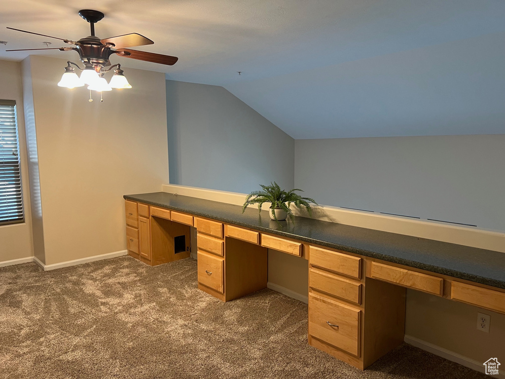Unfurnished office with a ceiling fan, lofted ceiling, dark carpet, built in study area, and baseboards