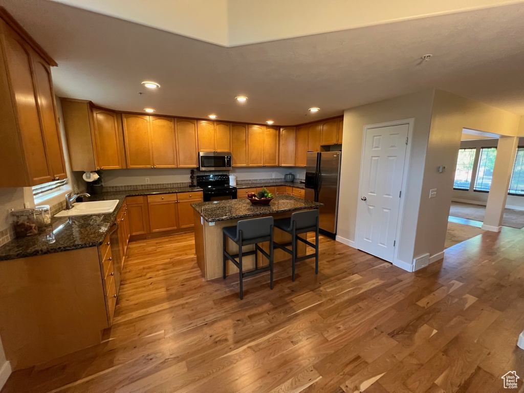Kitchen featuring stainless steel appliances, a sink, light wood-type flooring, a kitchen bar, and a center island