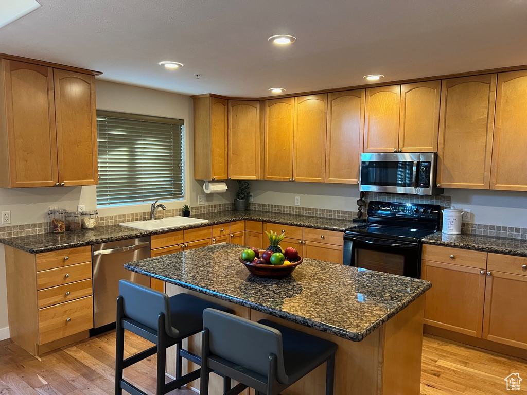 Kitchen featuring appliances with stainless steel finishes, a sink, light wood-style floors, a kitchen breakfast bar, and recessed lighting