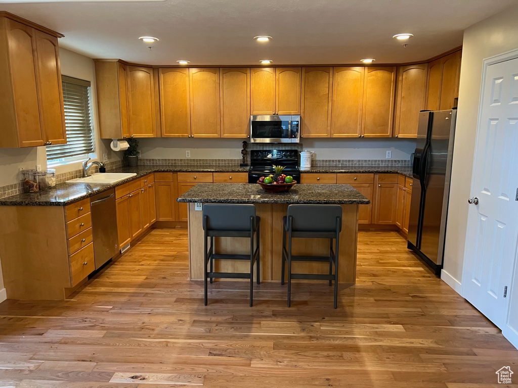 Kitchen featuring appliances with stainless steel finishes, a sink, light wood-style floors, a kitchen island, and recessed lighting