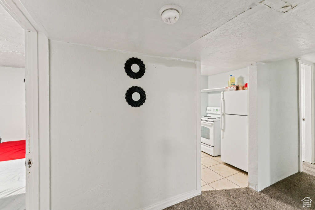 Hallway with light tile patterned flooring, light carpet, and a textured ceiling