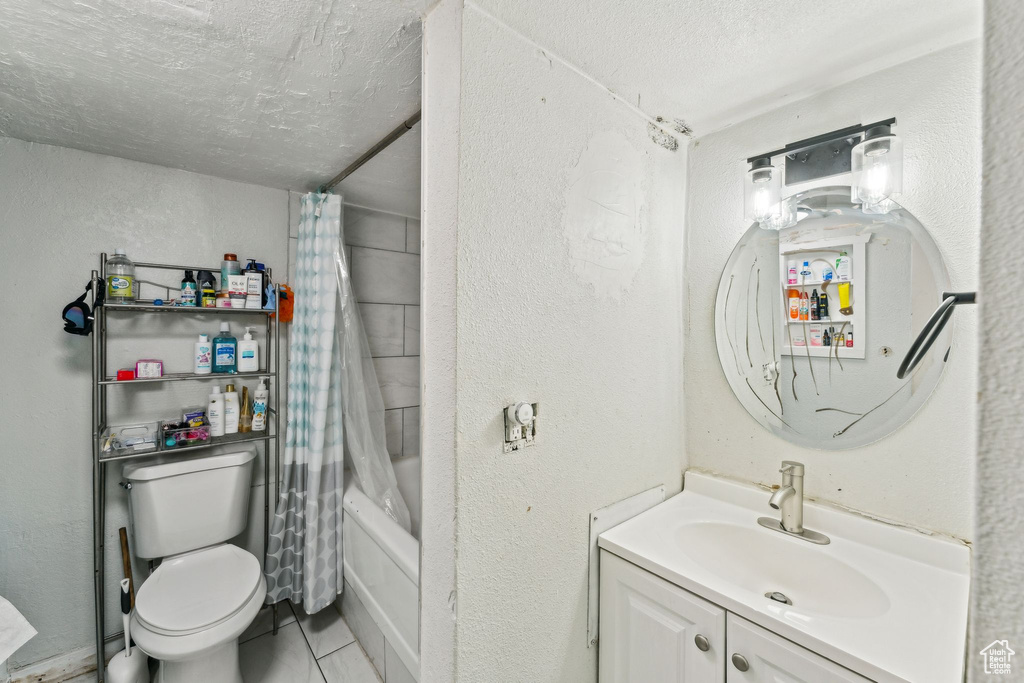 Full bathroom with a textured ceiling, vanity, toilet, a textured wall, and shower / tub combo with curtain