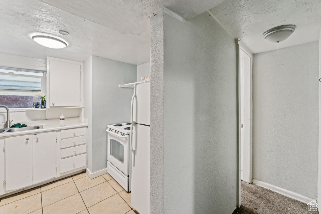 Kitchen featuring a sink, white appliances, white cabinets, a textured ceiling, and light countertops