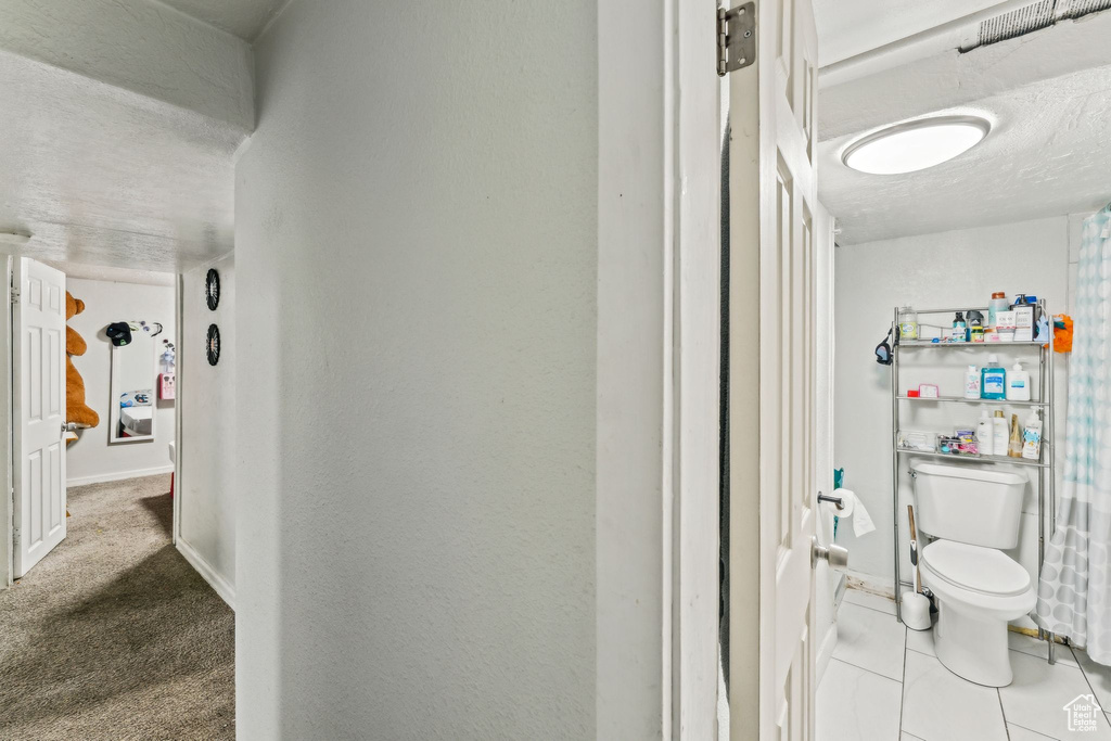 Hall with a textured ceiling, baseboards, and tile patterned flooring