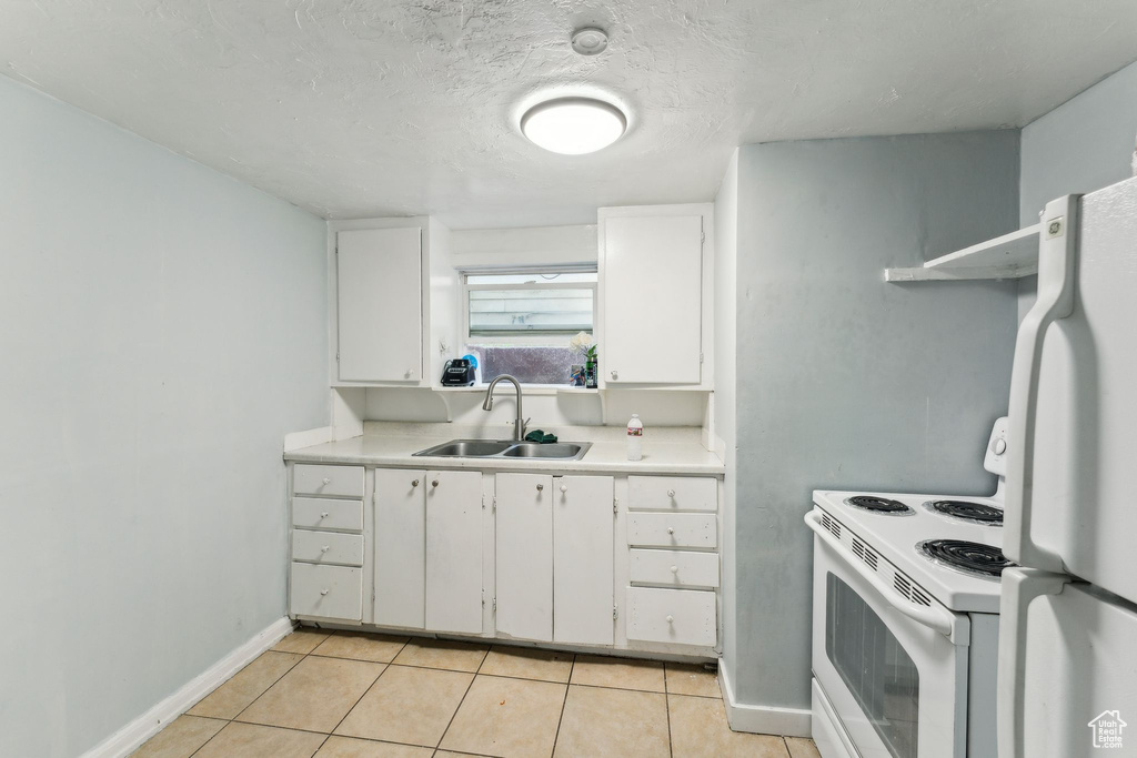 Kitchen with a sink, white appliances, light countertops, light tile patterned floors, and baseboards