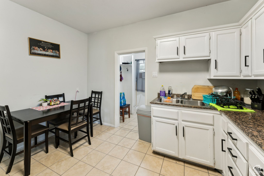Kitchen with a sink, dark countertops, light tile patterned floors, and white cabinetry