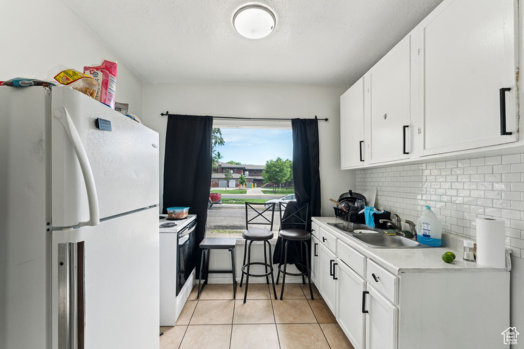 Kitchen featuring white appliances, light countertops, backsplash, and white cabinetry