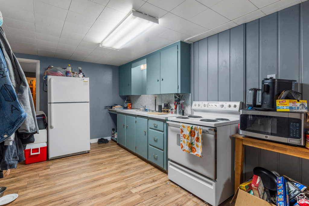 Kitchen with white appliances, blue cabinetry, light countertops, and light wood finished floors