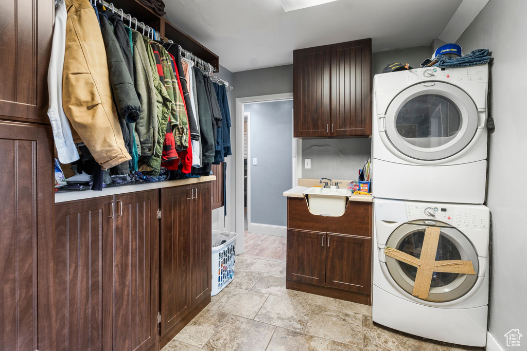 Clothes washing area featuring stacked washing machine and dryer, cabinet space, and baseboards