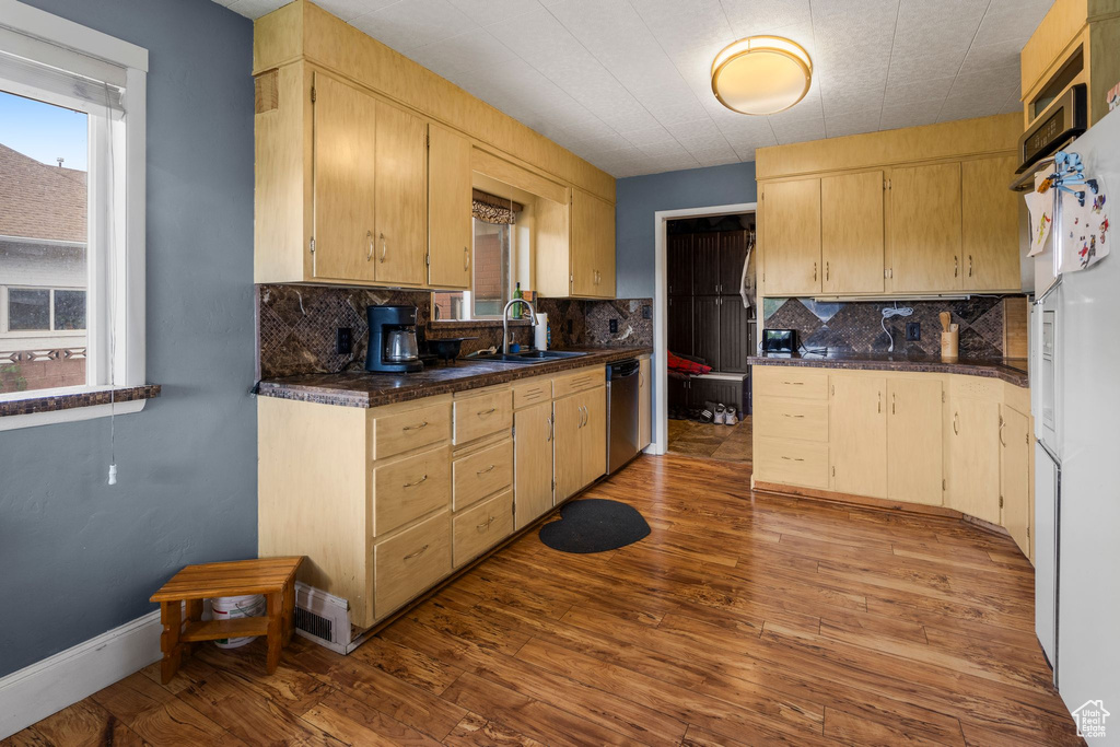 Kitchen featuring a sink, dishwasher, backsplash, dark countertops, and wood finished floors