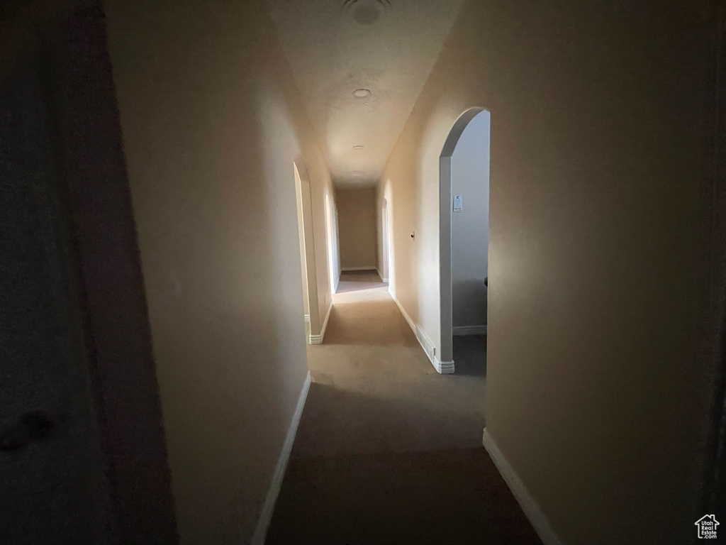 Hallway with arched walkways, baseboards, and carpet flooring