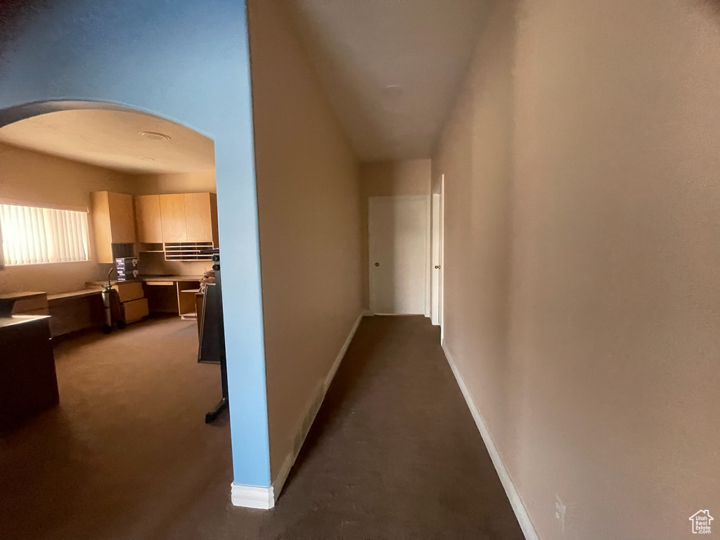 Corridor with arched walkways, baseboards, and dark carpet