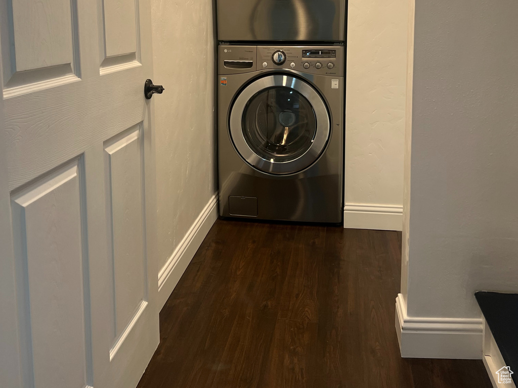 Laundry area with stacked washer / dryer, dark wood-type flooring, and baseboards
