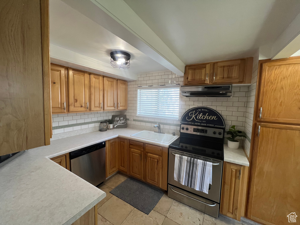Kitchen featuring appliances with stainless steel finishes, a sink, ventilation hood, tasteful backsplash, and light countertops