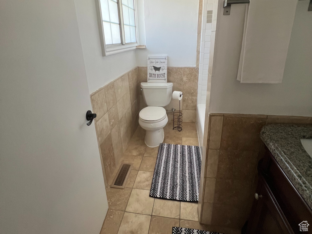 Bathroom with tile walls, tile patterned flooring, vanity, toilet, and a wainscoted wall