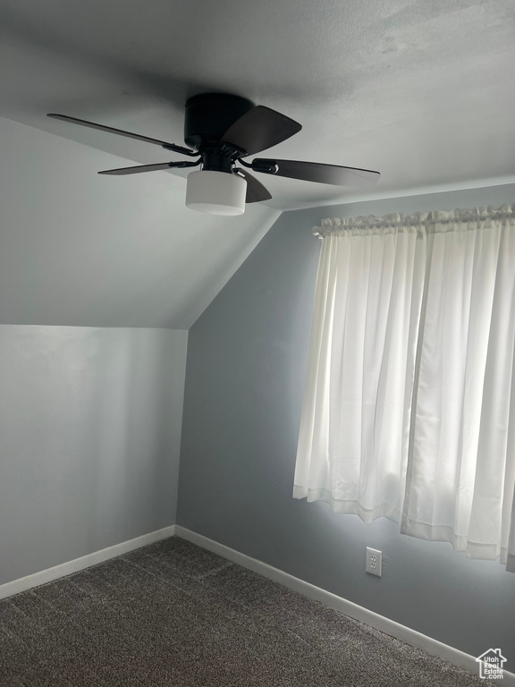 Additional living space featuring ceiling fan, vaulted ceiling, baseboards, and dark colored carpet