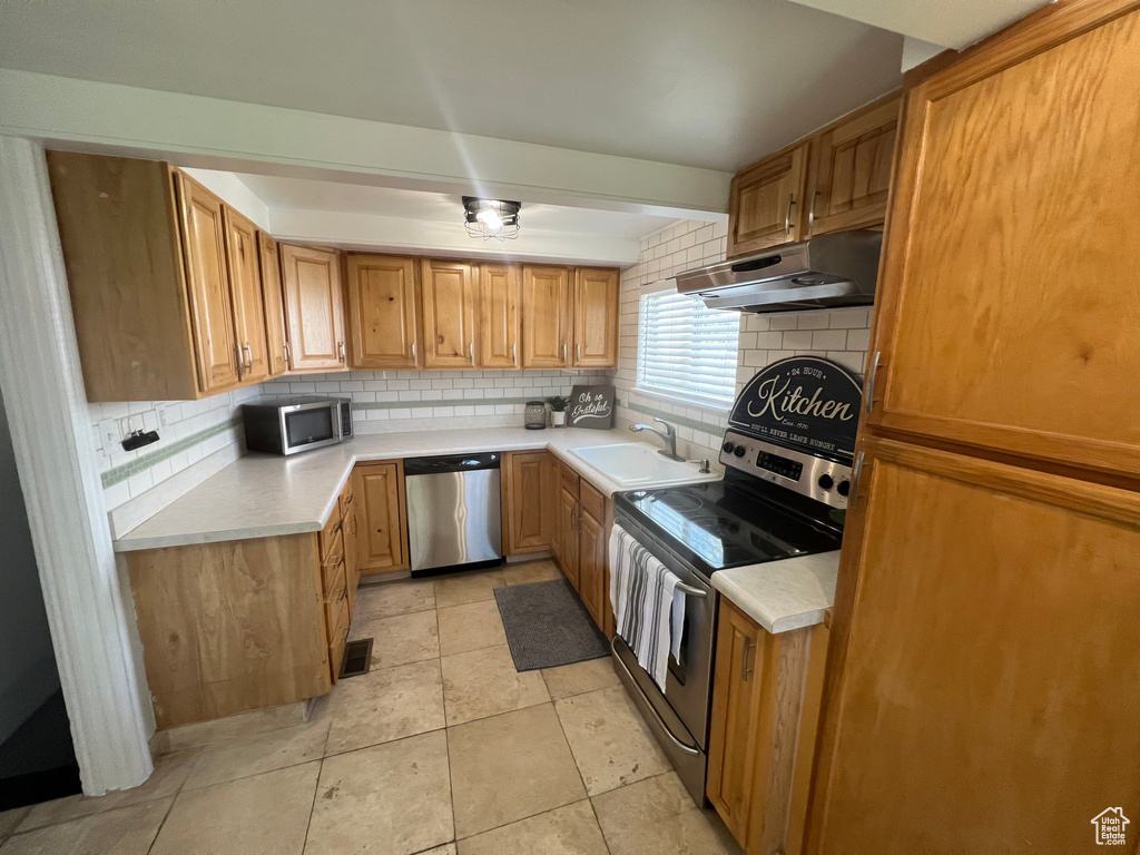 Kitchen with appliances with stainless steel finishes, under cabinet range hood, tasteful backsplash, and light countertops
