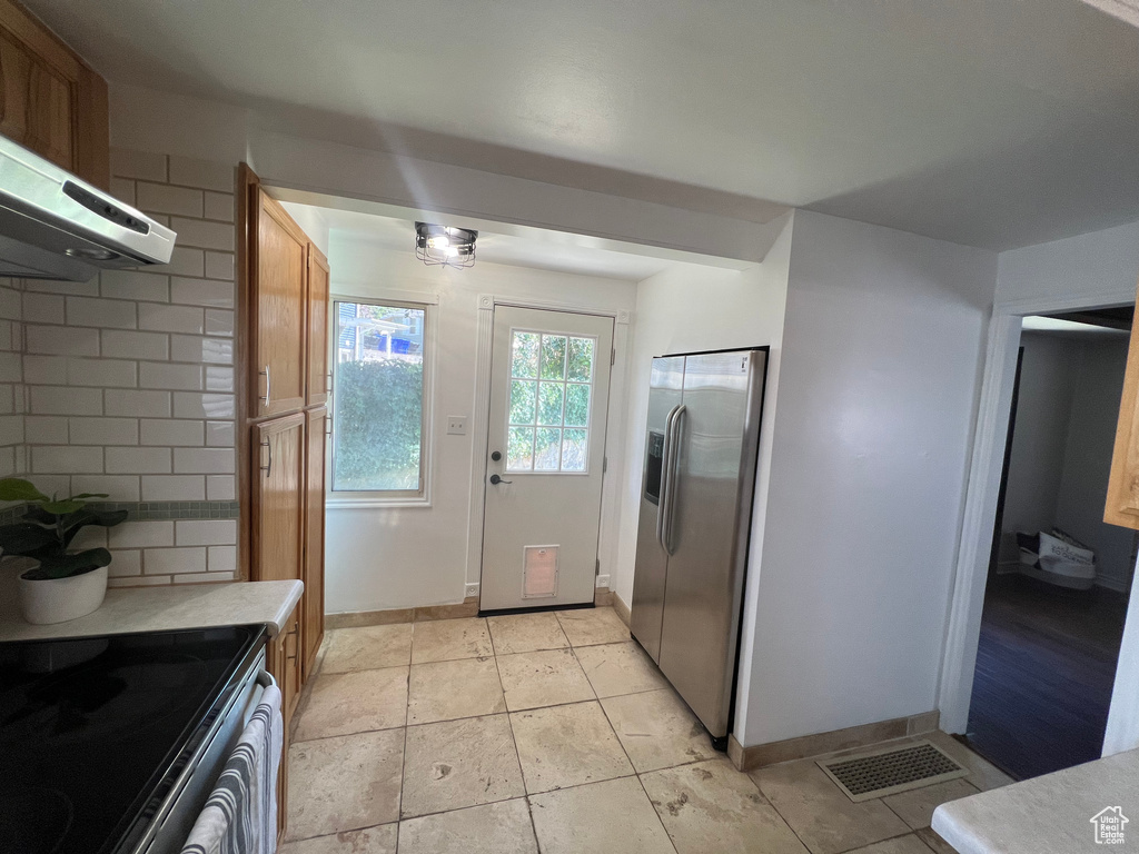 Kitchen featuring stainless steel appliances, range hood, light countertops, decorative backsplash, and brown cabinets