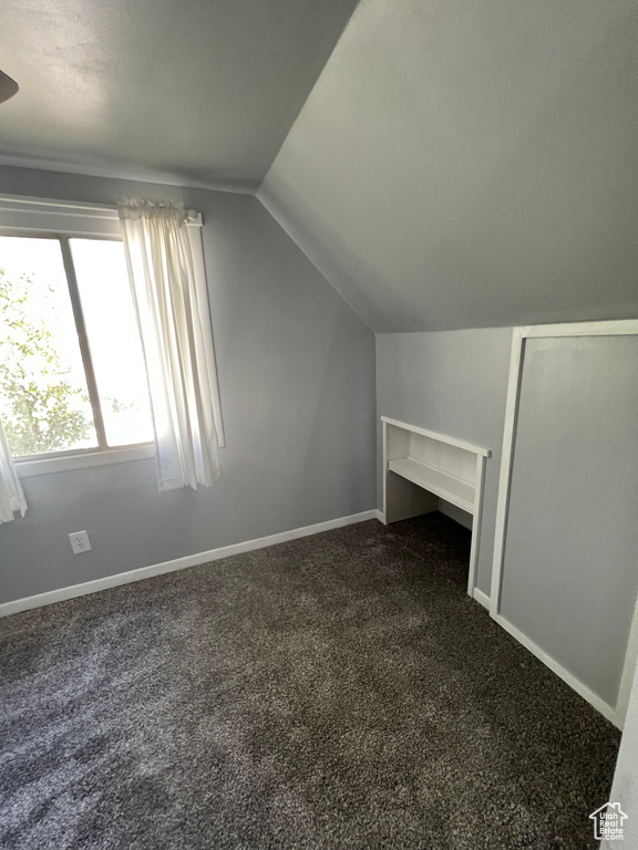 Bonus room featuring vaulted ceiling, dark carpet, and baseboards