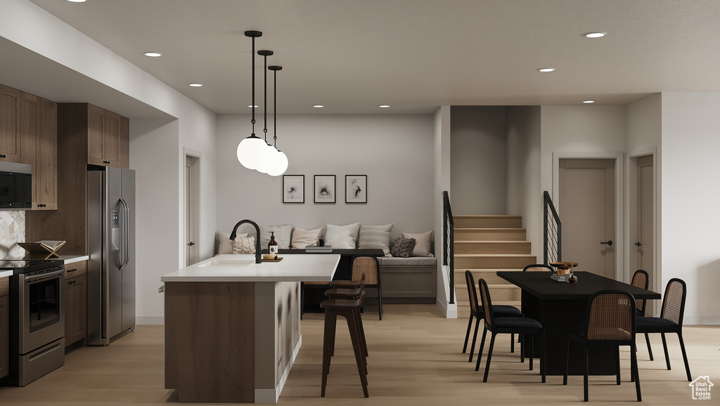 Kitchen with appliances with stainless steel finishes, a sink, light wood-style floors, recessed lighting, and a center island with sink
