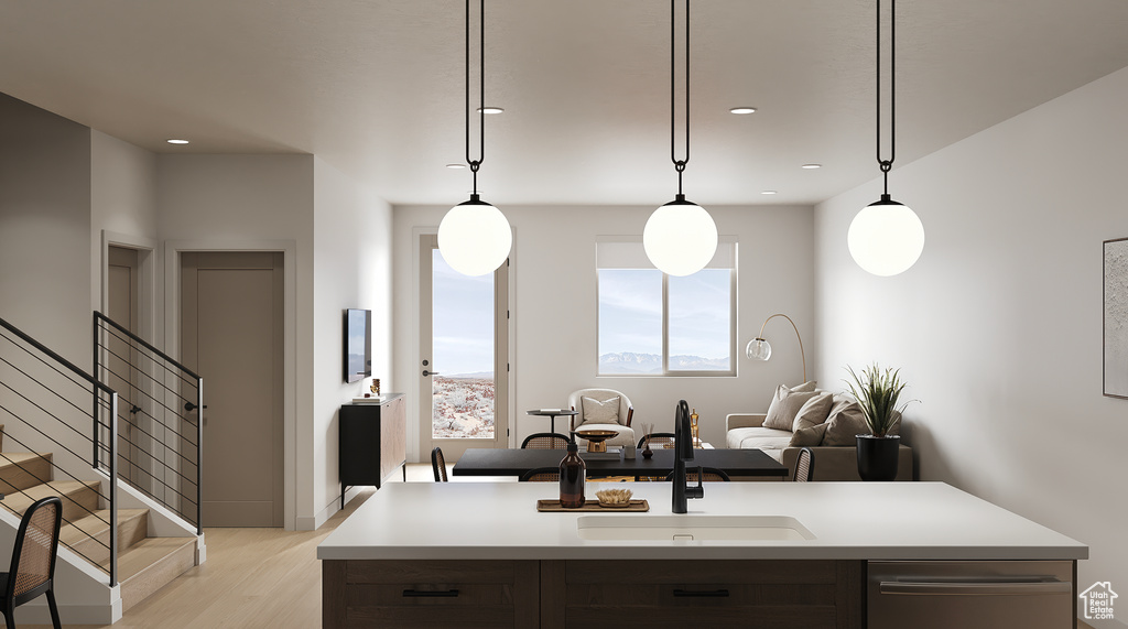 Kitchen with a sink, light countertops, light wood-style floors, stainless steel dishwasher, and decorative light fixtures