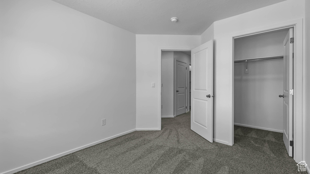 Unfurnished bedroom featuring dark colored carpet, baseboards, a closet, and a spacious closet