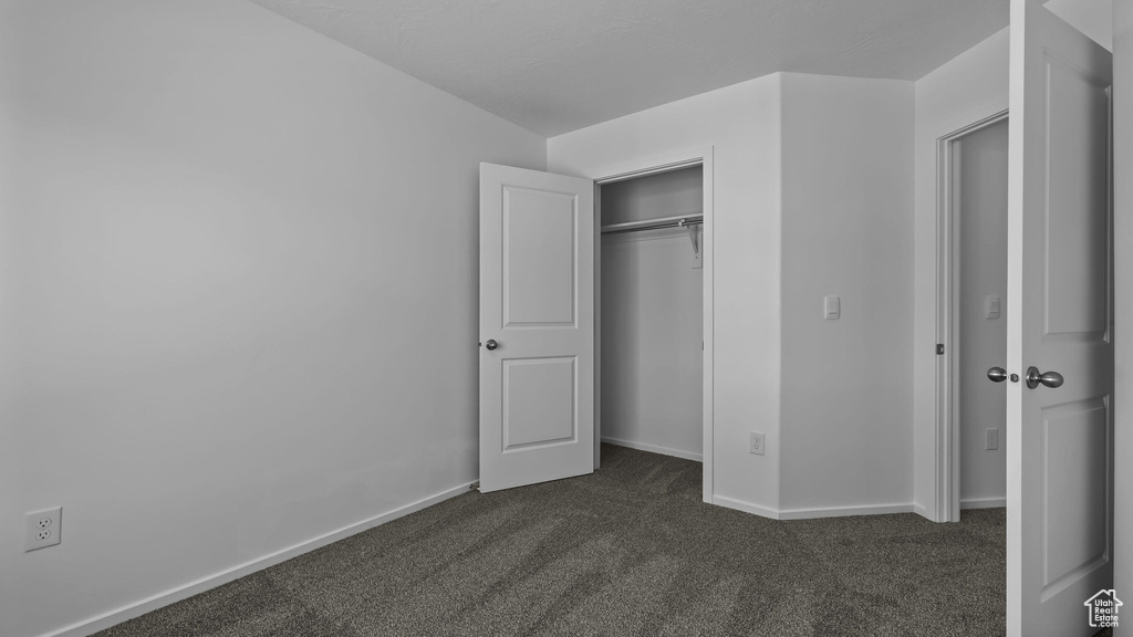 Unfurnished bedroom featuring dark colored carpet, baseboards, and a closet