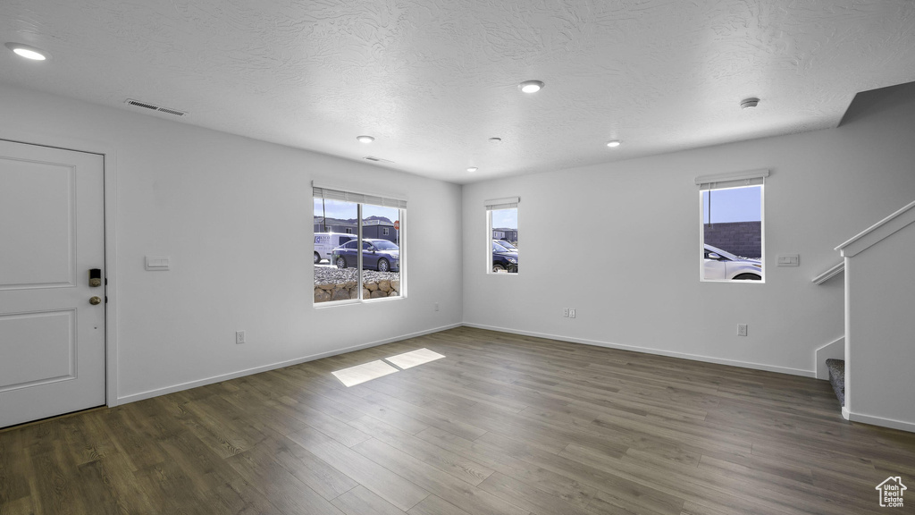 Unfurnished living room featuring plenty of natural light, stairs, wood finished floors, a textured ceiling, and recessed lighting