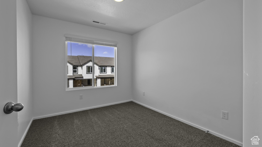 Spare room featuring dark colored carpet and baseboards