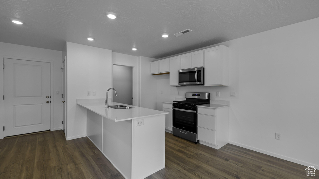 Kitchen with appliances with stainless steel finishes, a sink, a peninsula, dark wood finished floors, and baseboards
