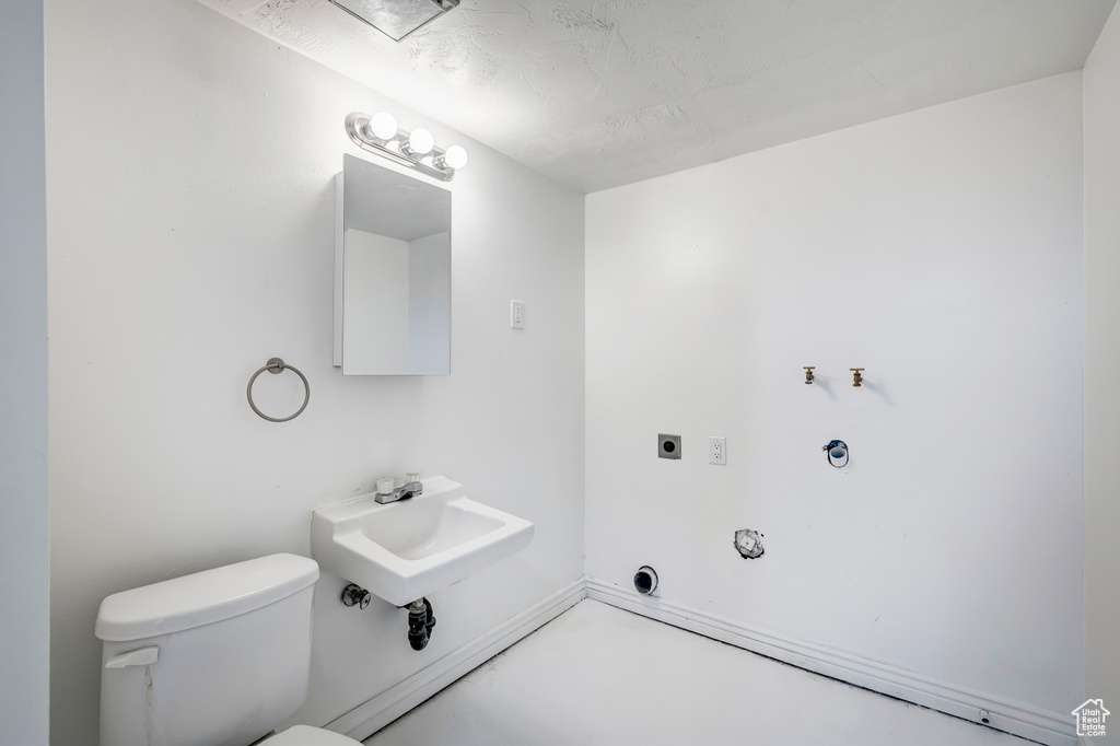 Half bathroom with toilet, a sink, and concrete flooring