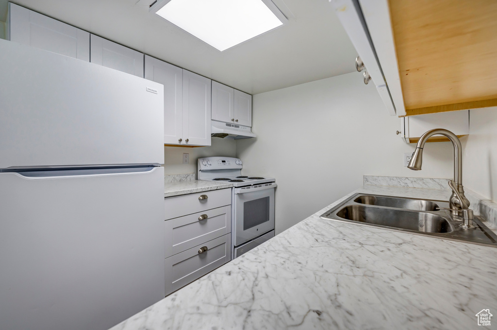 Kitchen featuring freestanding refrigerator, white range with electric cooktop, a sink, under cabinet range hood, and white cabinetry