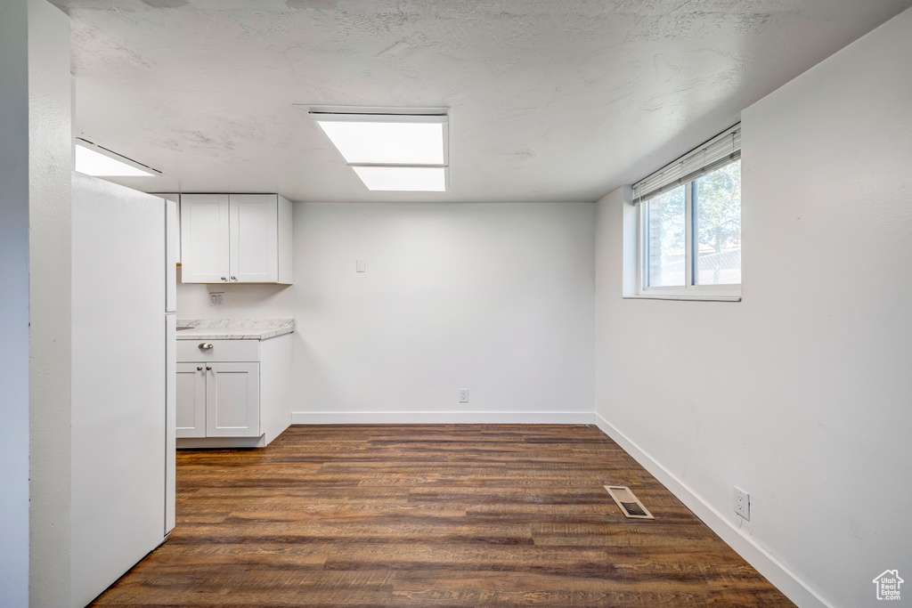 Basement with freestanding refrigerator, baseboards, and dark wood-type flooring
