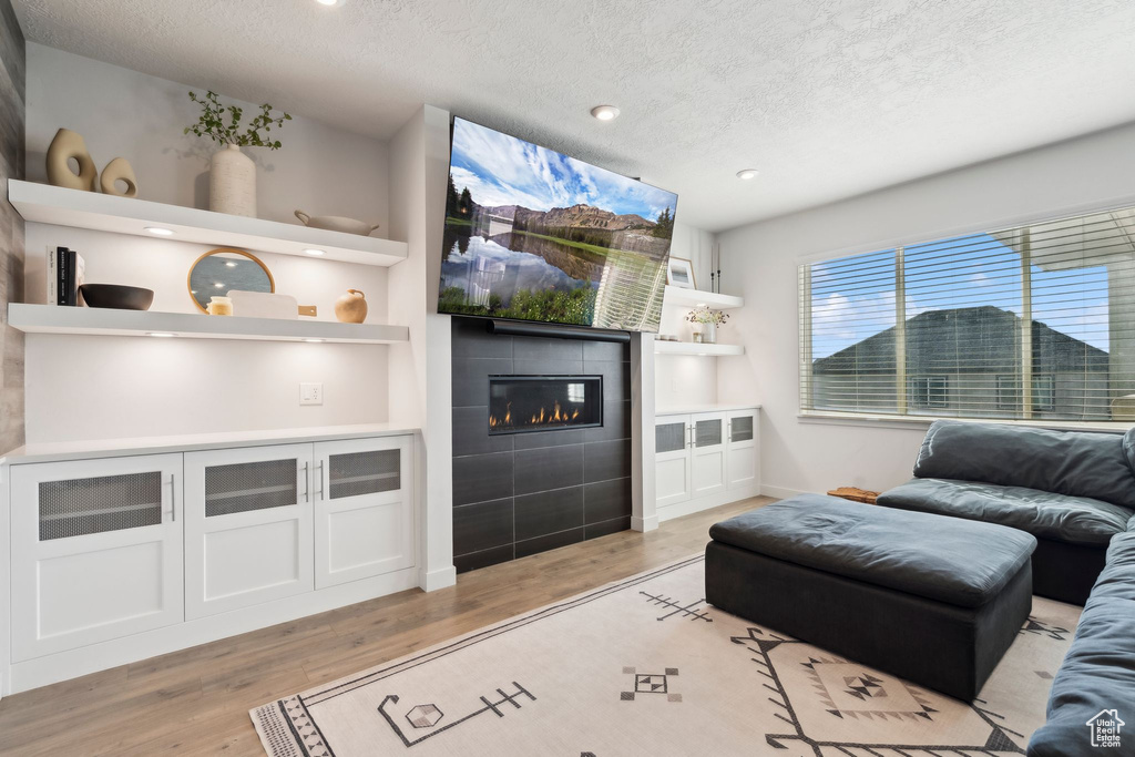 Living area featuring a fireplace, a textured ceiling, light wood-type flooring, recessed lighting, and baseboards