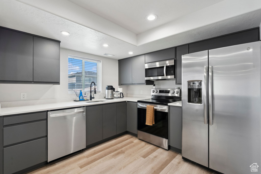 Kitchen with stainless steel appliances, a sink, gray cabinets, light wood-style flooring, and recessed lighting