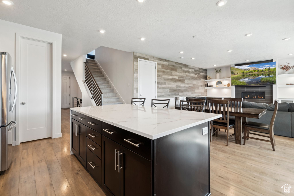 Kitchen with stainless steel fridge, light wood-style flooring, light stone countertops, a kitchen island, and open floor plan