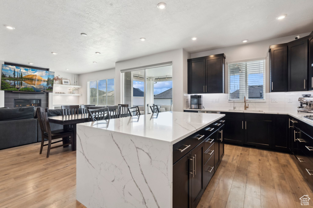 Kitchen with a sink, light wood-style flooring, a kitchen island, open floor plan, and backsplash