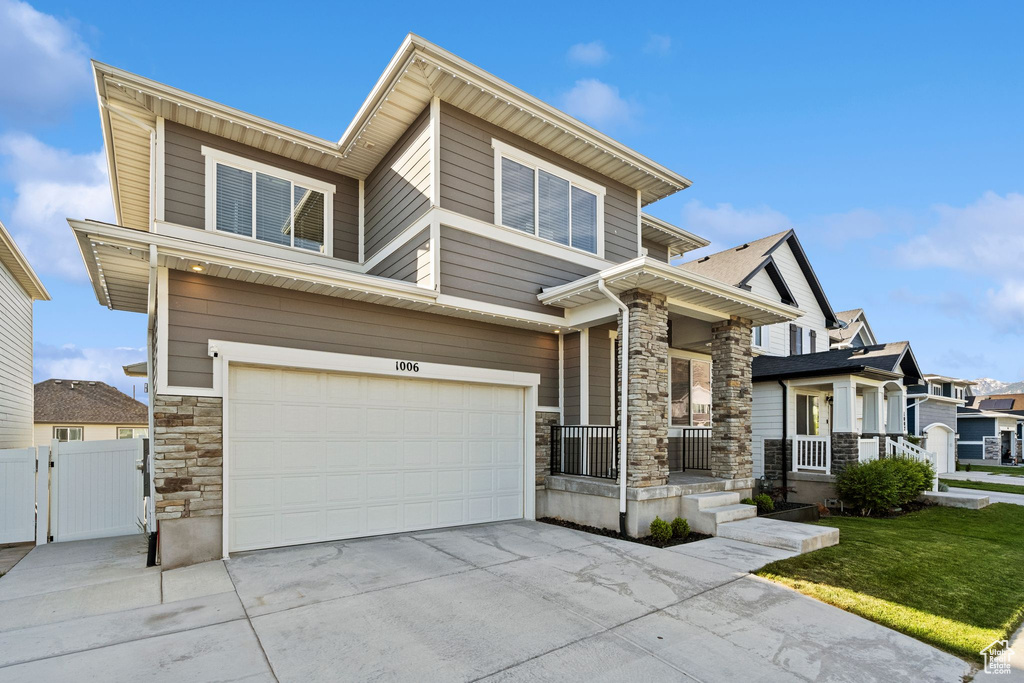 View of front of home with stone siding, a porch, an attached garage, driveway, and a gate