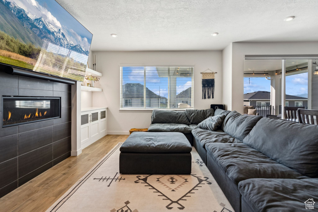 Living room featuring light wood-style flooring, a tile fireplace, baseboards, a textured ceiling, and recessed lighting