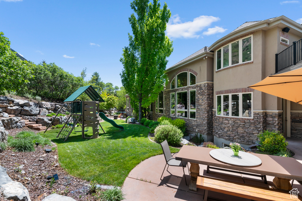 View of green lawn featuring a playground, a patio, and outdoor dining area