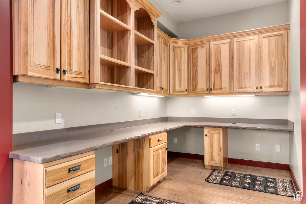 Unfurnished office featuring built in desk, light wood-style flooring, and baseboards