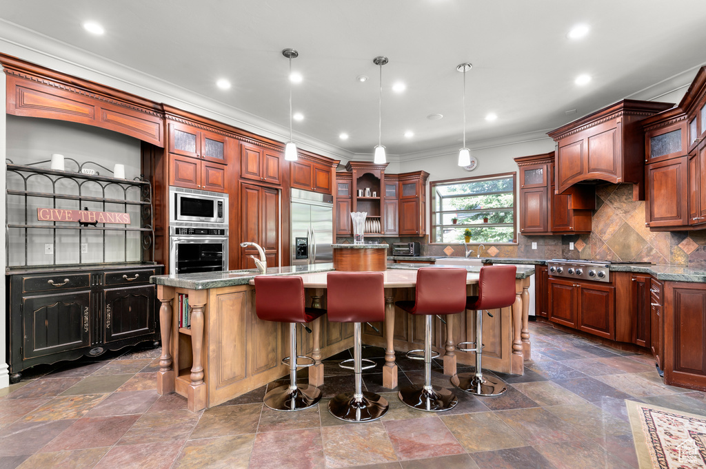 Kitchen with built in appliances, a center island with sink, ornamental molding, open shelves, and tasteful backsplash