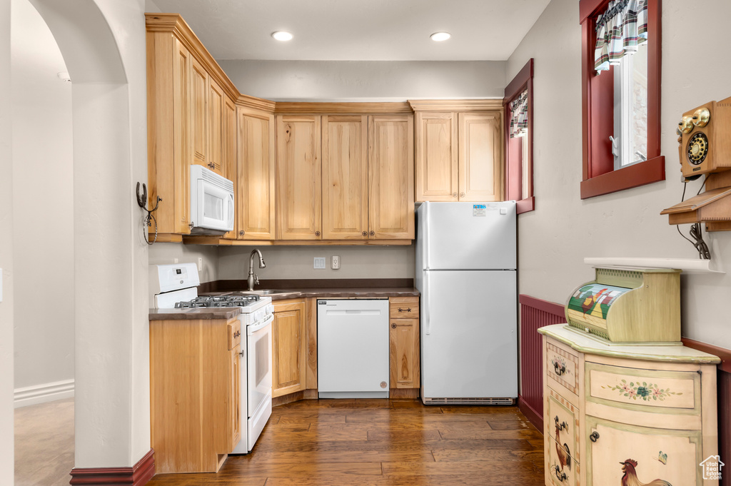 Kitchen with white appliances, dark countertops, dark wood-type flooring, a sink, and arched walkways